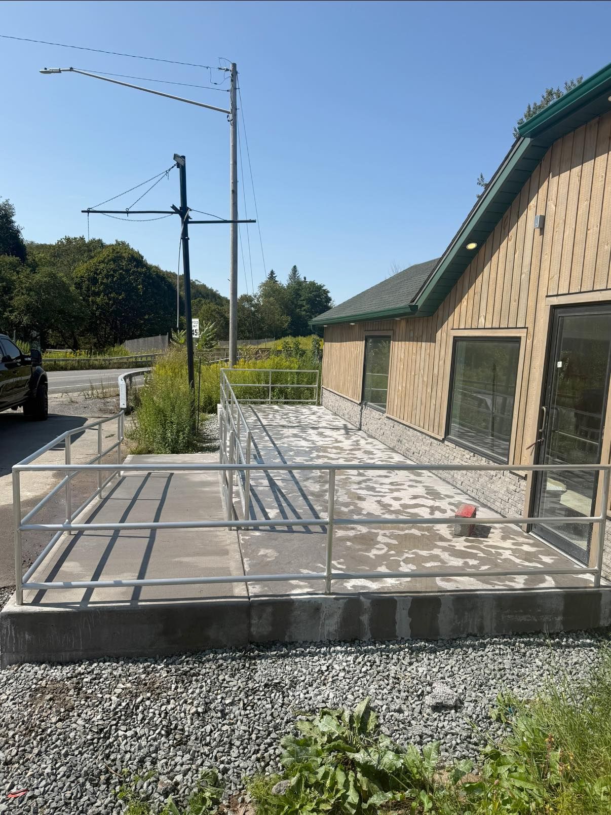 A building with a ramp and railing, featuring a concrete patio and gravel.