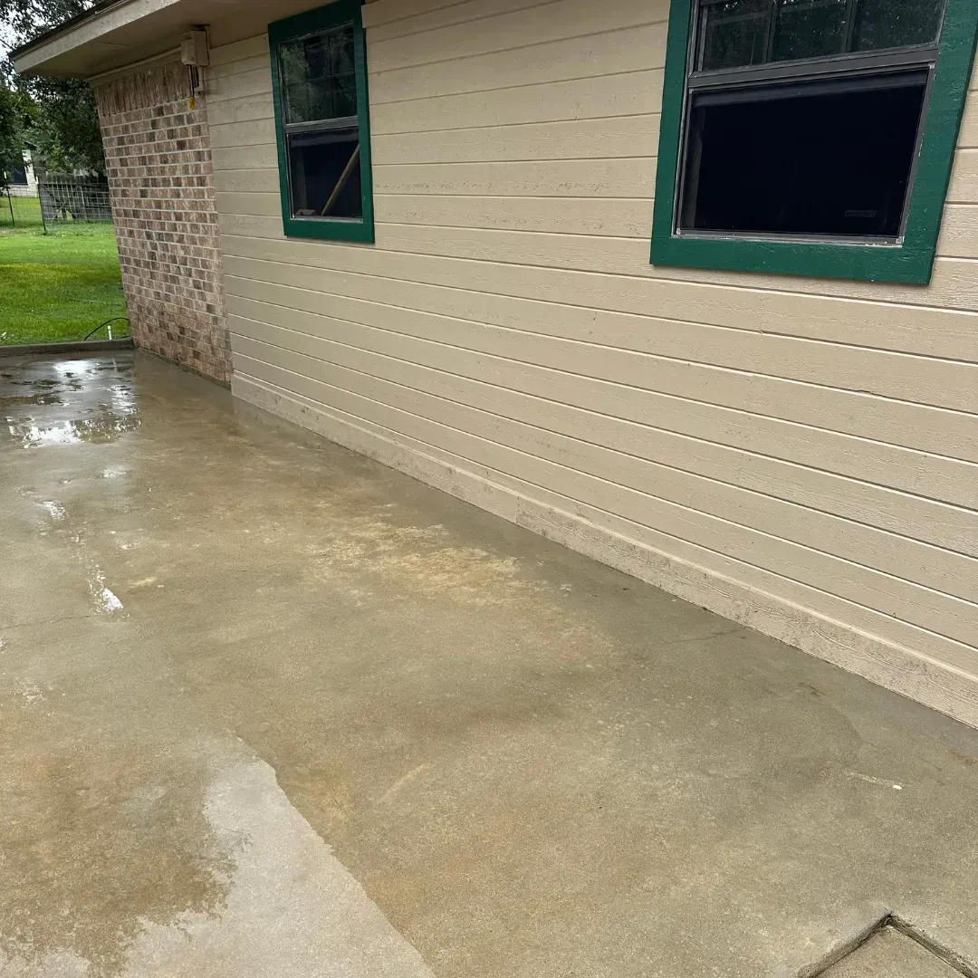 A white house with green windows and a concrete driveway in front of it.