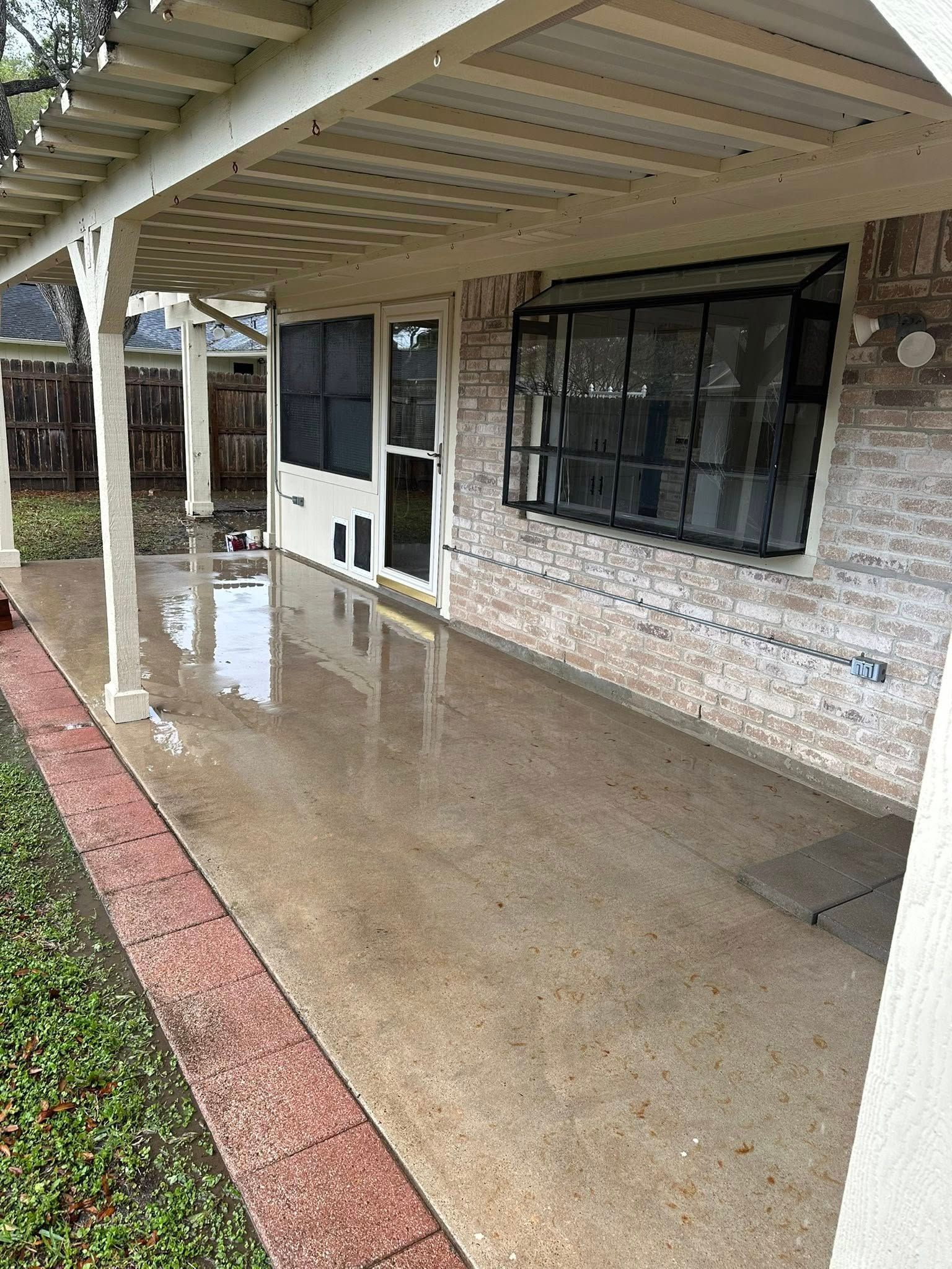A patio with a covered area and a window on the side of a house.