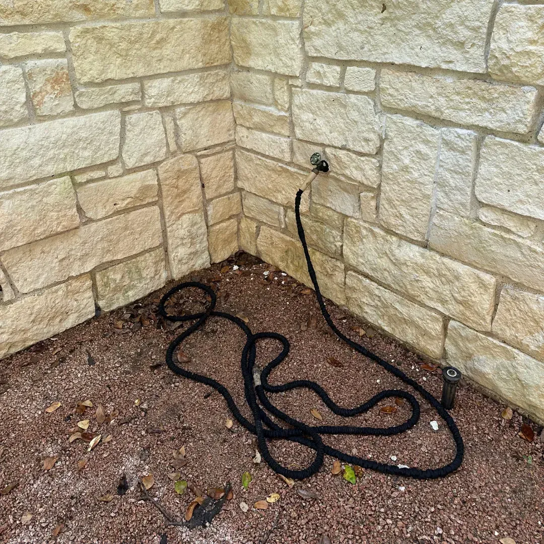 A hose is laying on the ground in front of a brick wall.