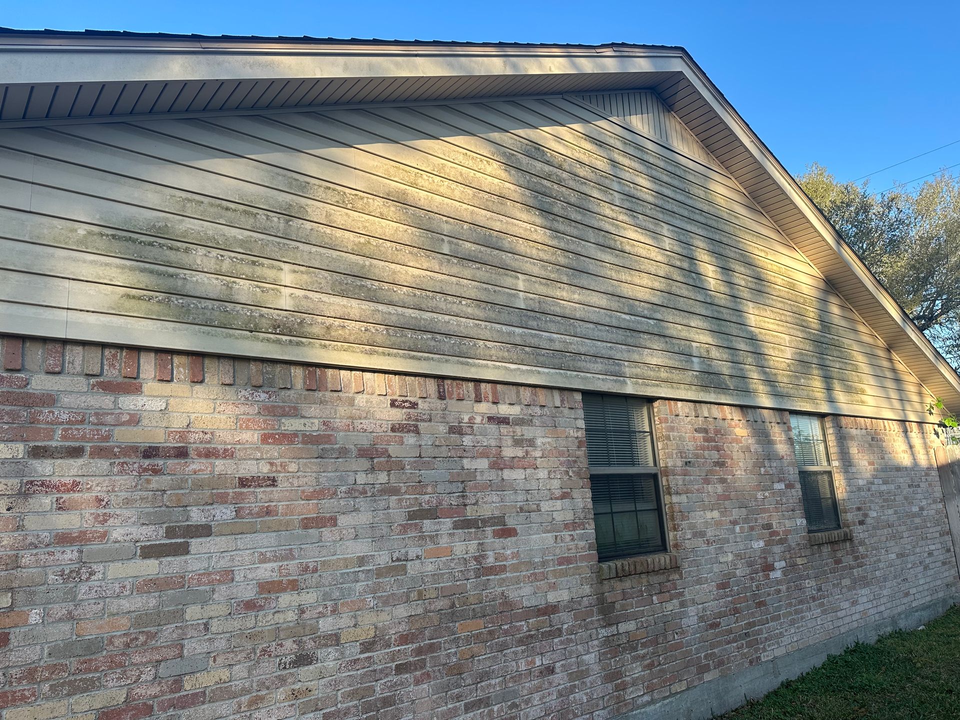 A brick house with a white siding and two windows.