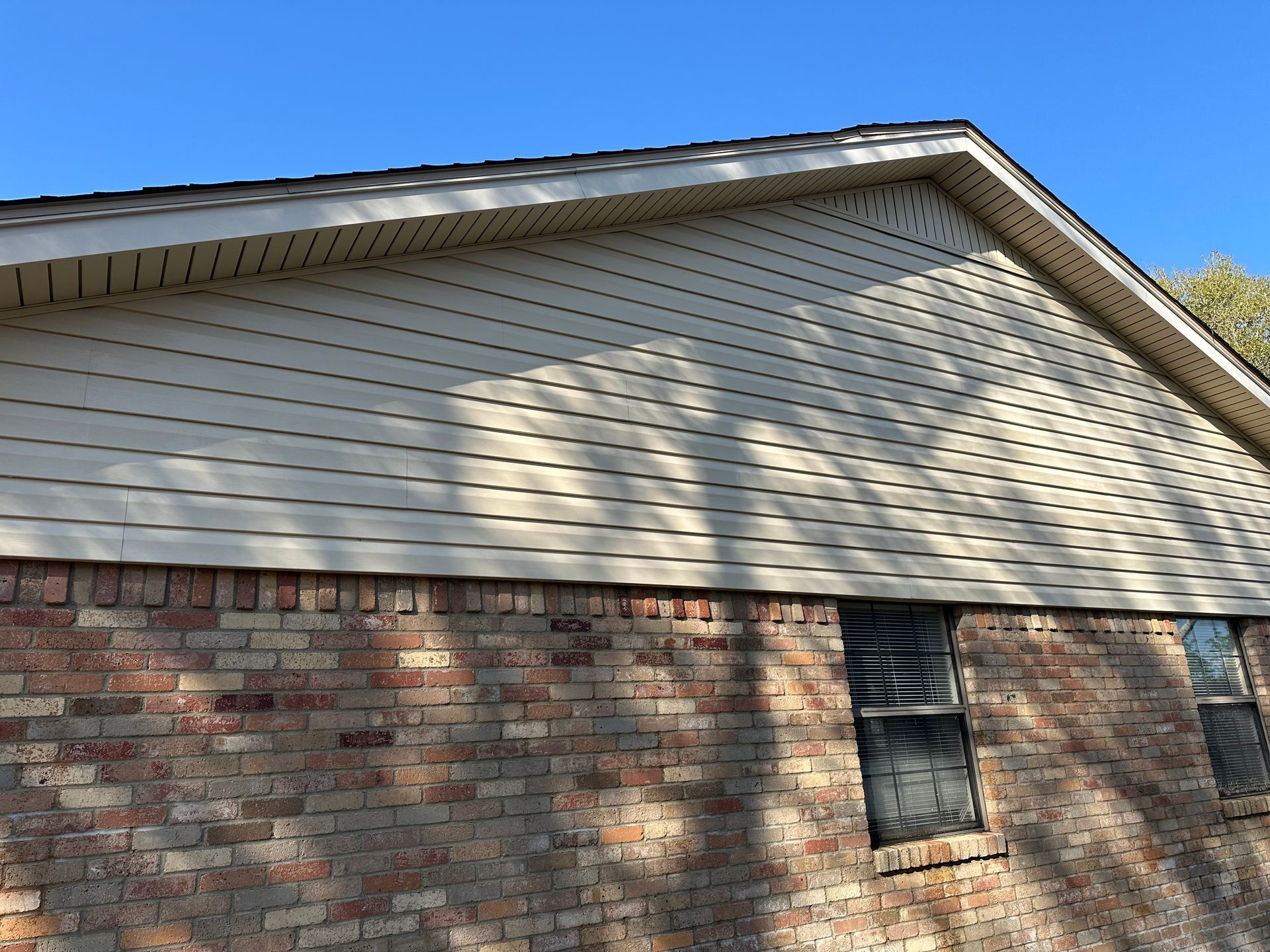 A brick house with white siding and a blue sky in the background.