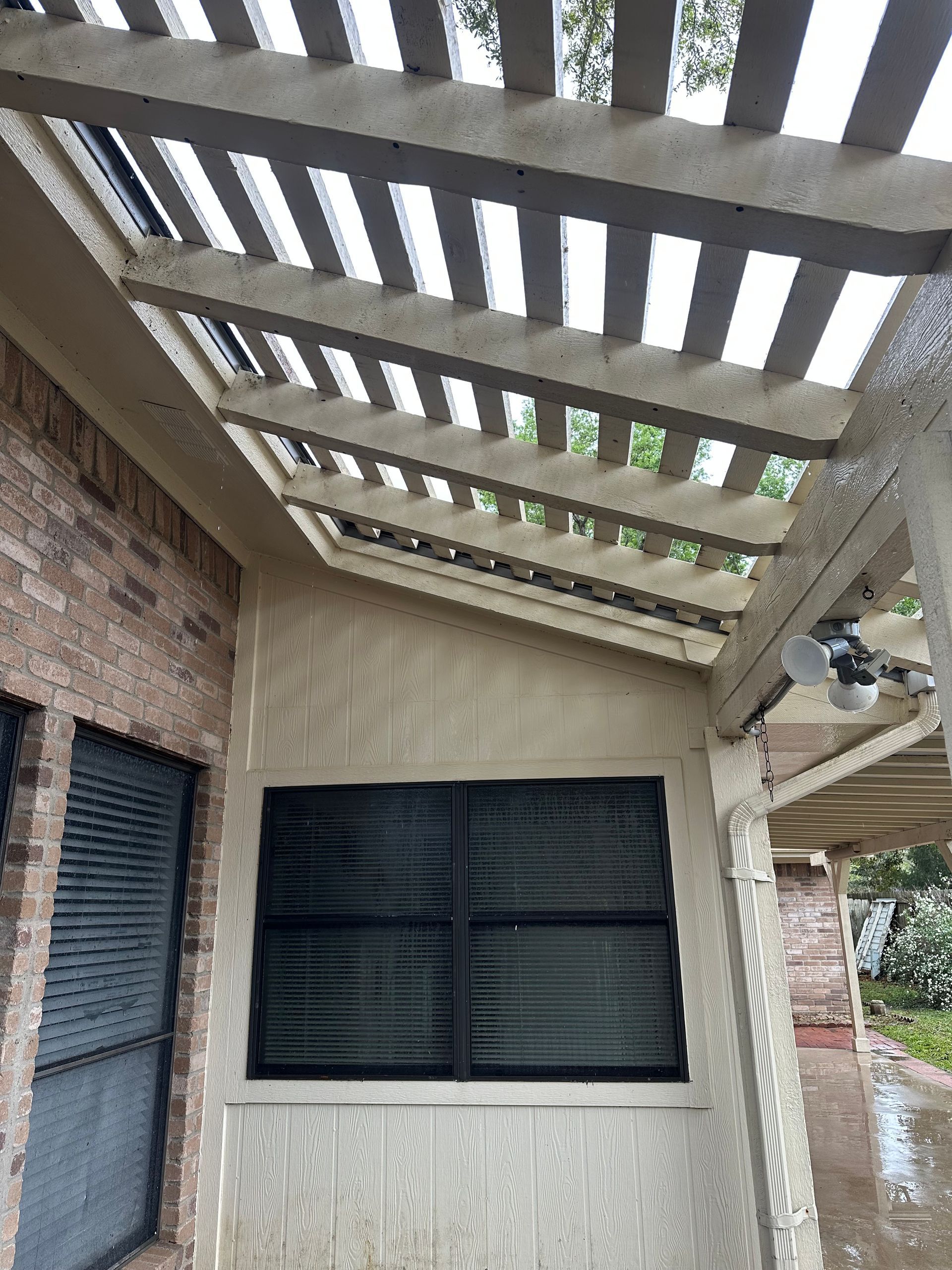A pergola over a window on the side of a house.
