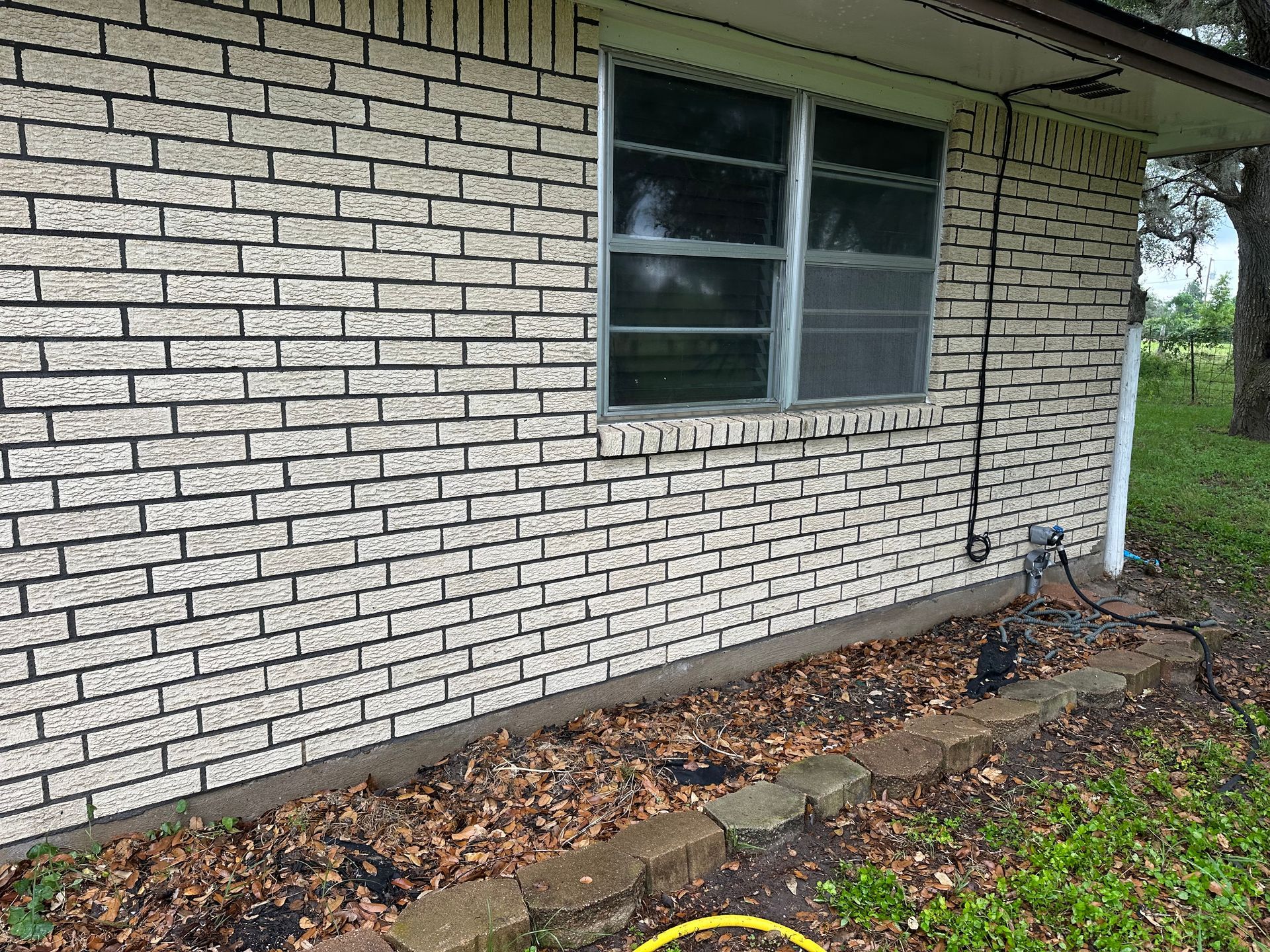 A white brick house with a window and a hose in front of it.