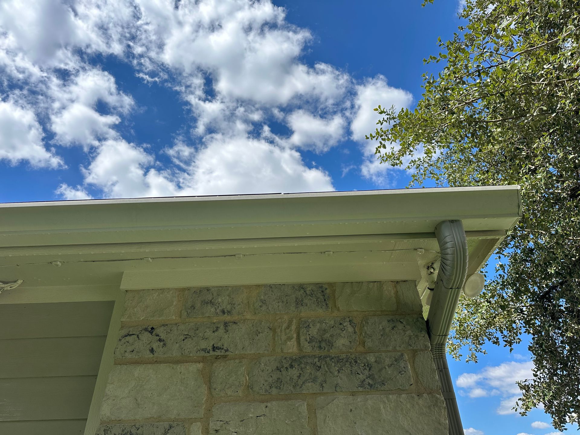 The roof of a house with a tree in the background and a blue sky with clouds.