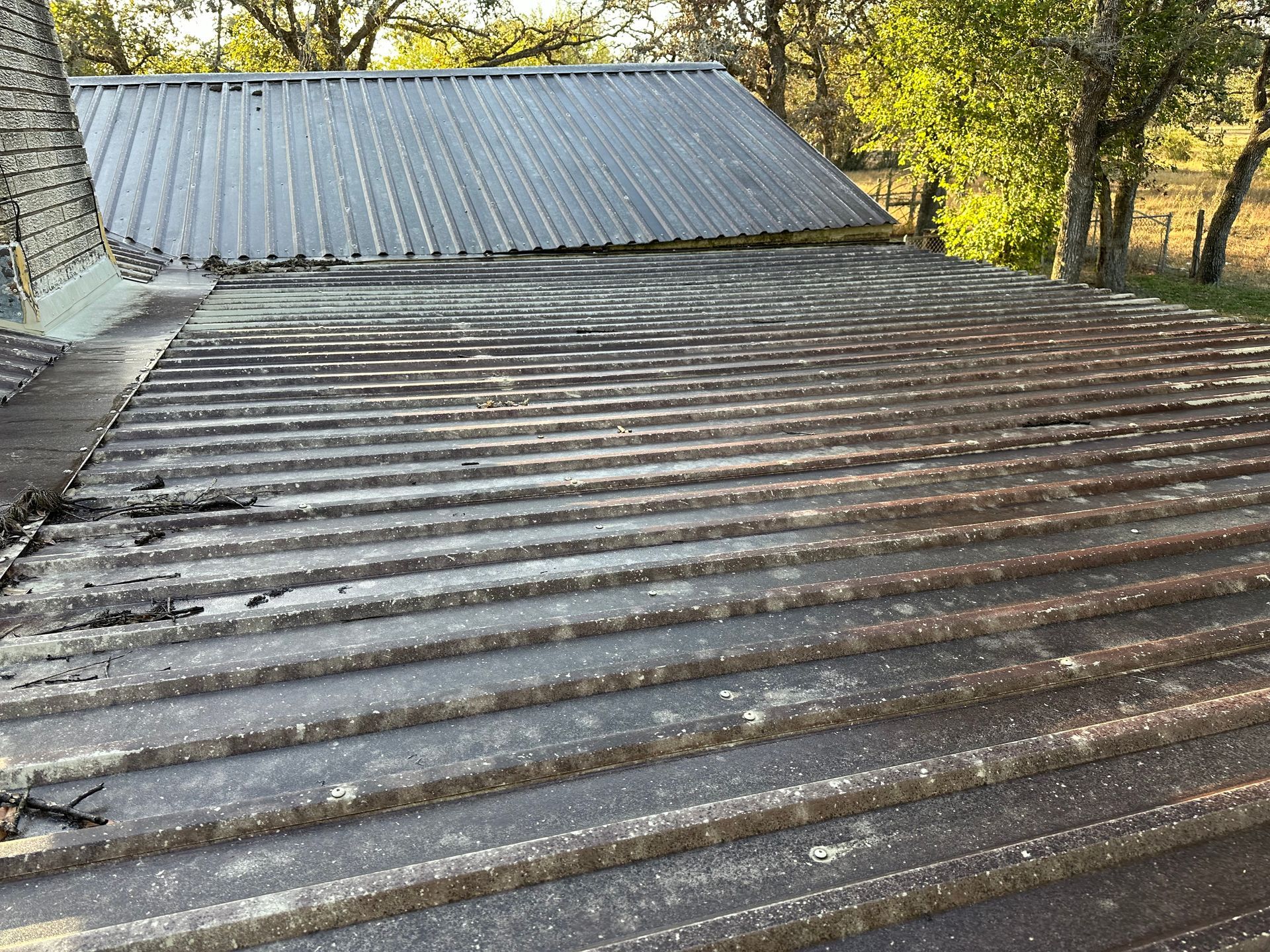 A rusty metal roof with a chimney and trees in the background.