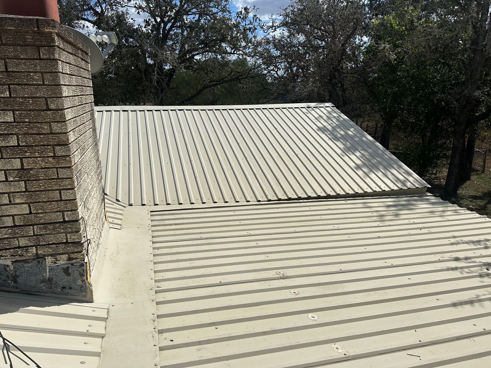 A white metal roof with a brick chimney on top of it.
