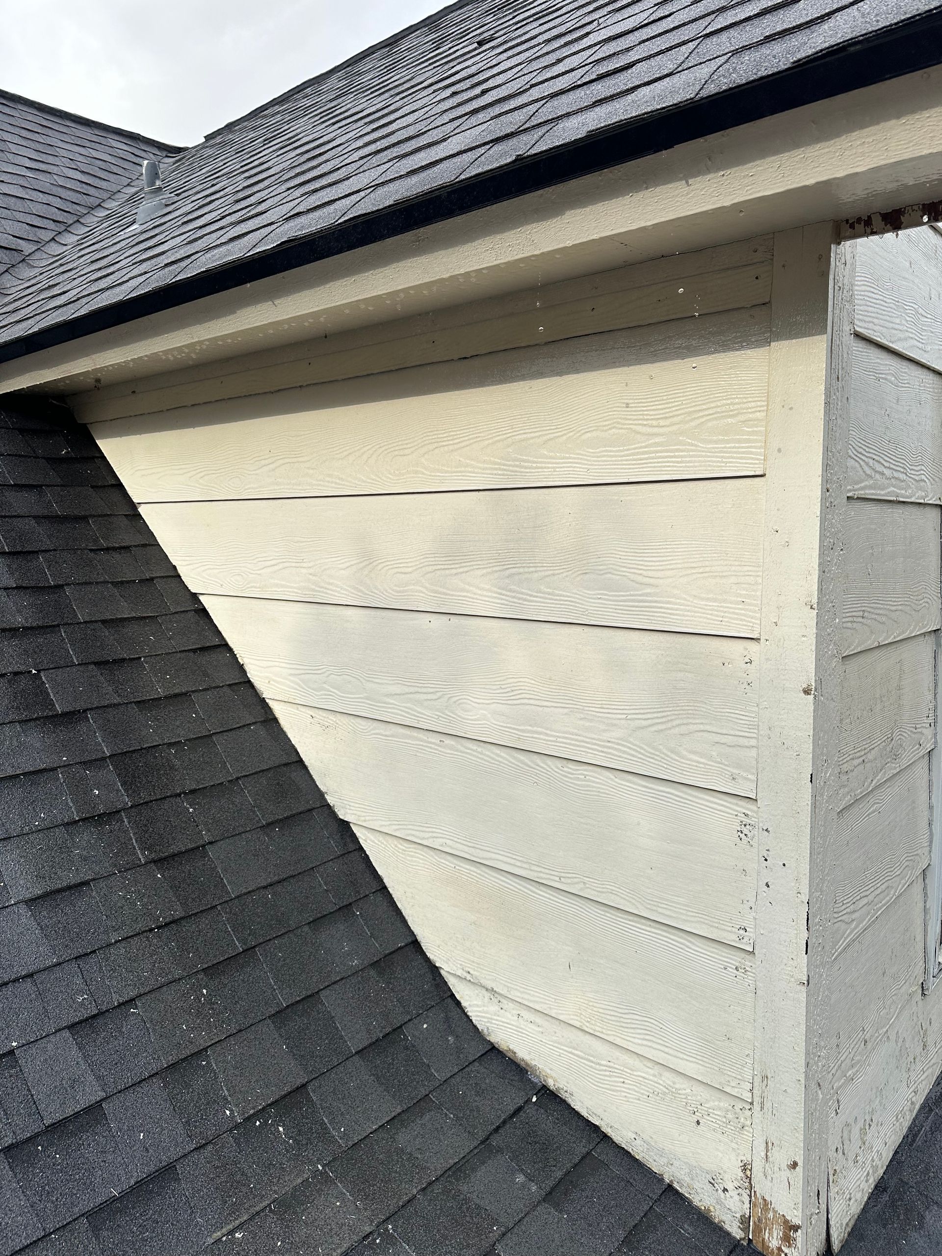 A close up of a roof with a white siding and a black roof.