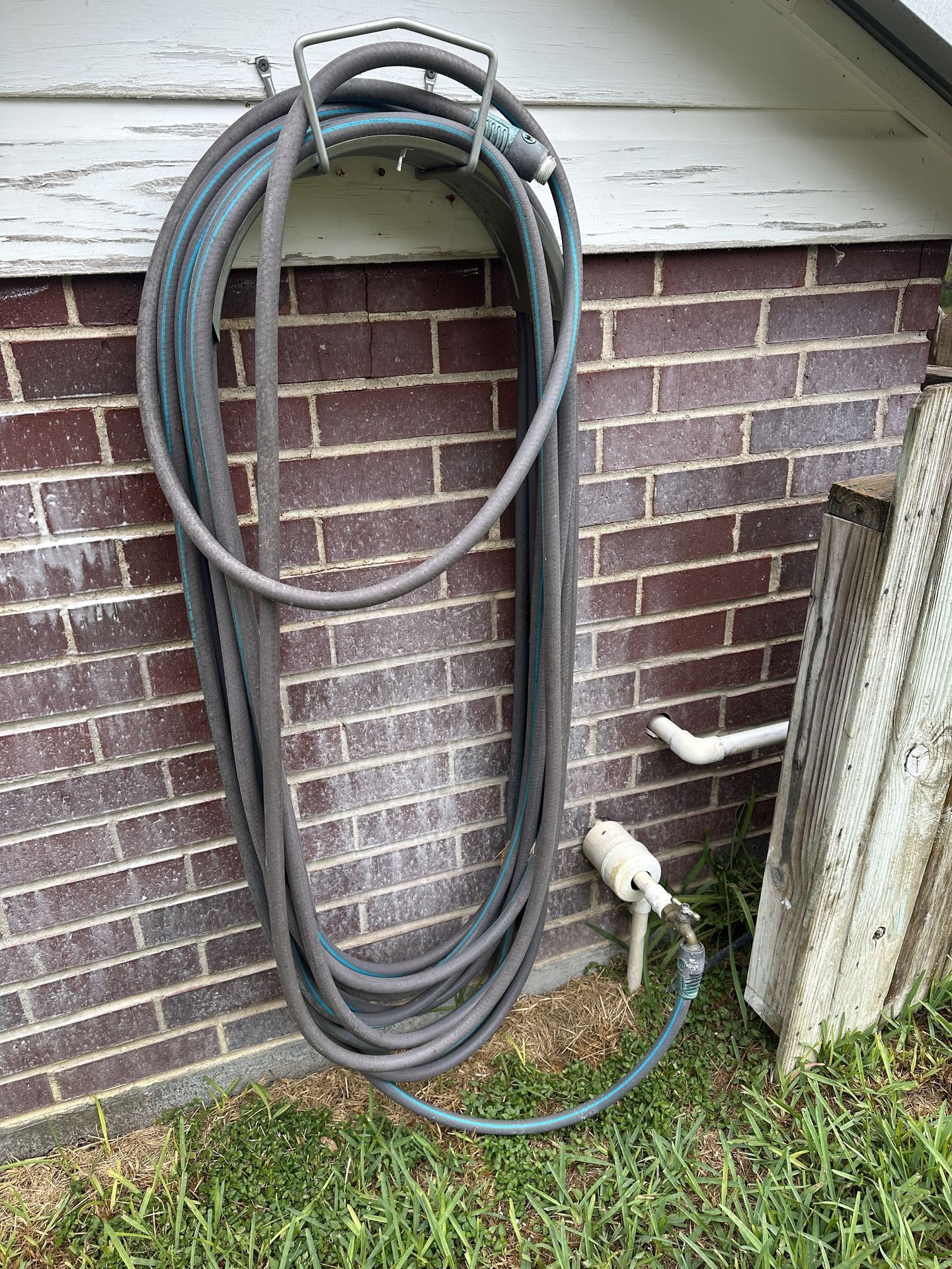 A hose is hanging on the side of a brick wall.
