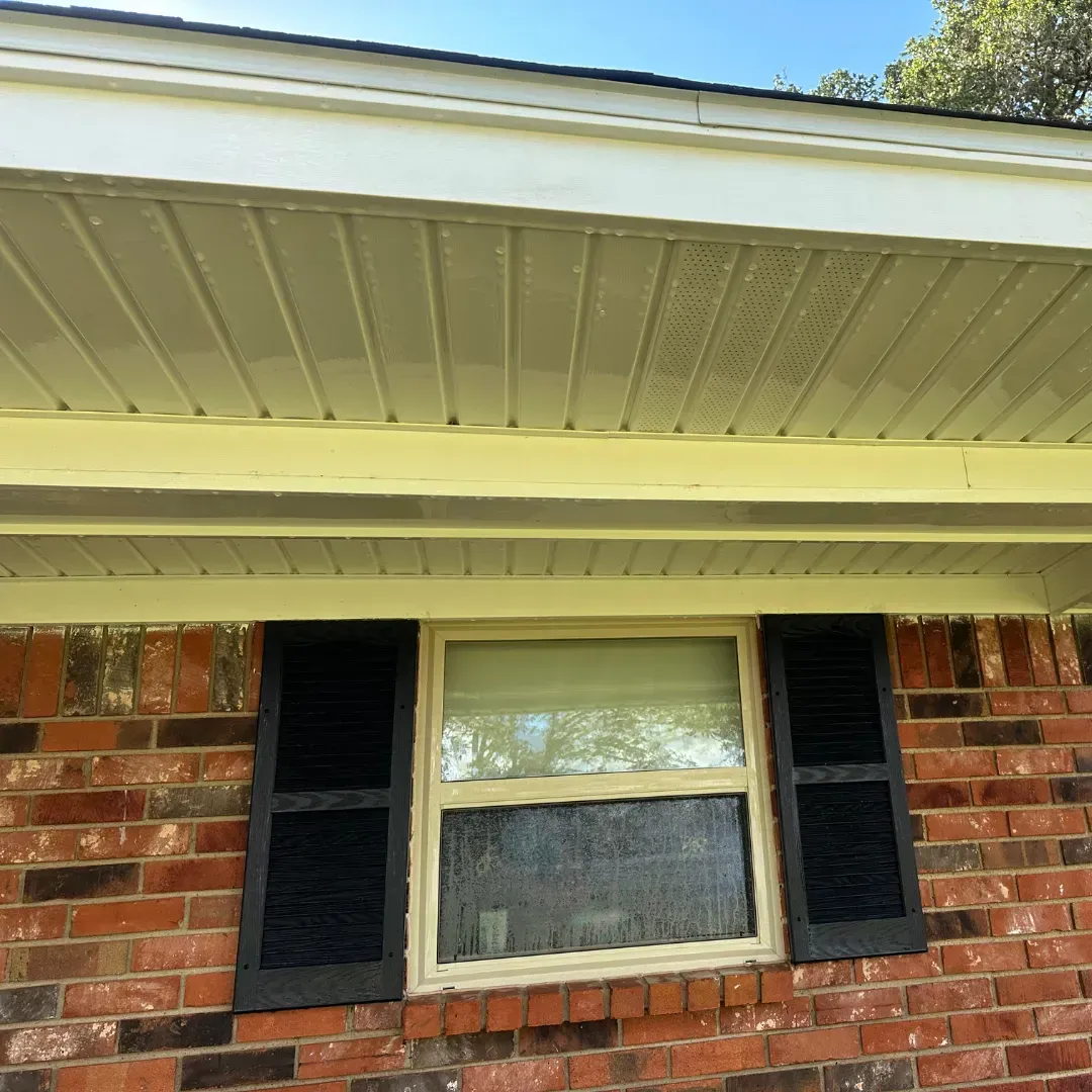 A brick house with a window and black shutters on it.