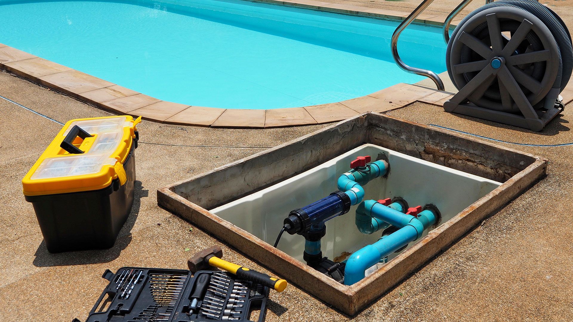Pool pump and pipes within a concrete access pit, with tools and toolbox nearby.