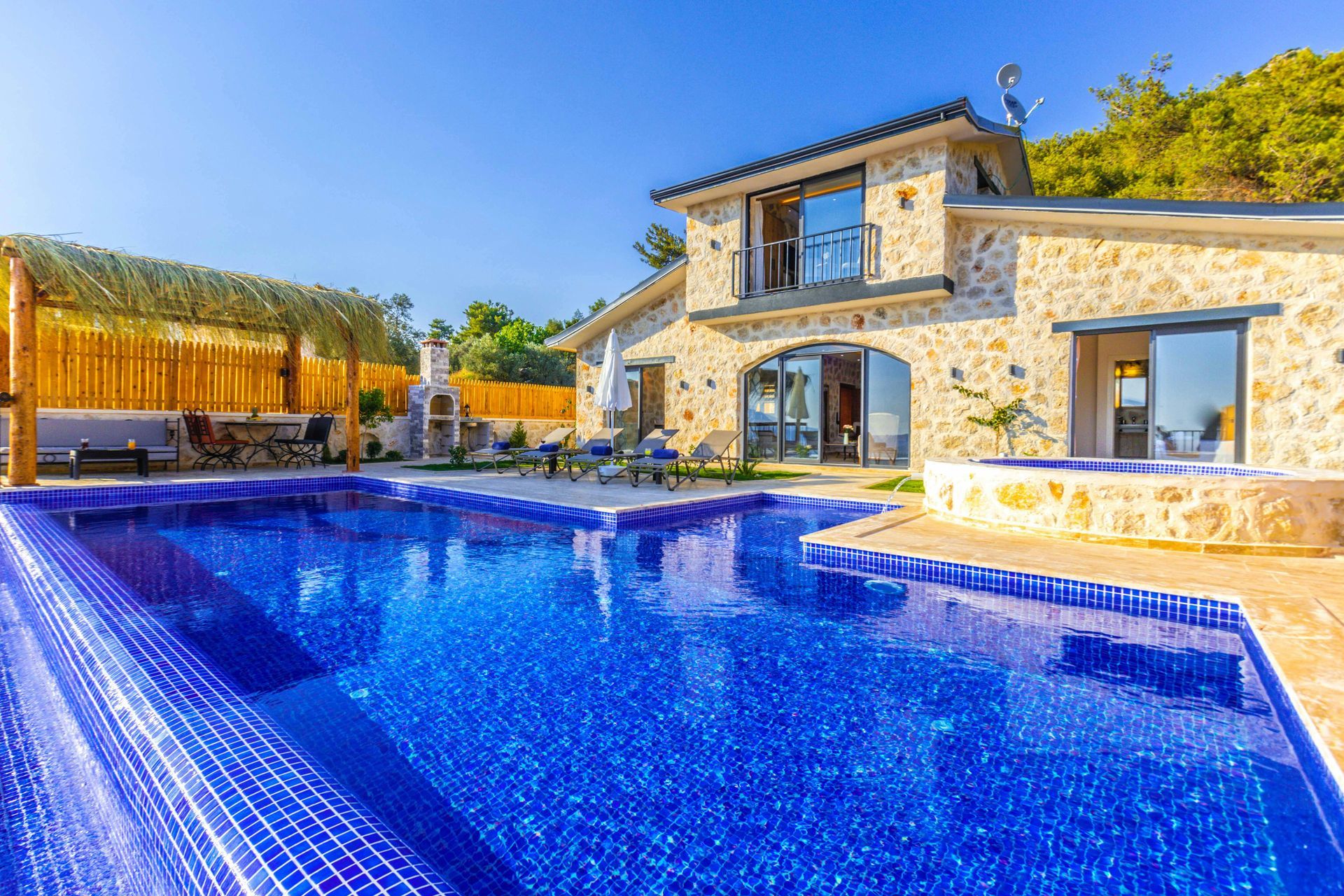 Luxurious villa with blue pool, stone facade, jacuzzi, and outdoor dining area.