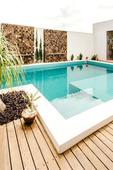 Pool with turquoise water, white edges, wooden deck, and stone accent wall.
