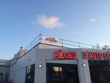 Un bâtiment blanc avec des lettres rouges sur lesquelles est écrit pièces d auto le