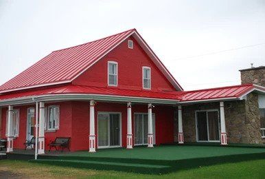 Une maison rouge avec un toit rouge et un porche vert