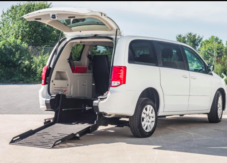 A white van with a ramp attached to the back is parked in a parking lot.