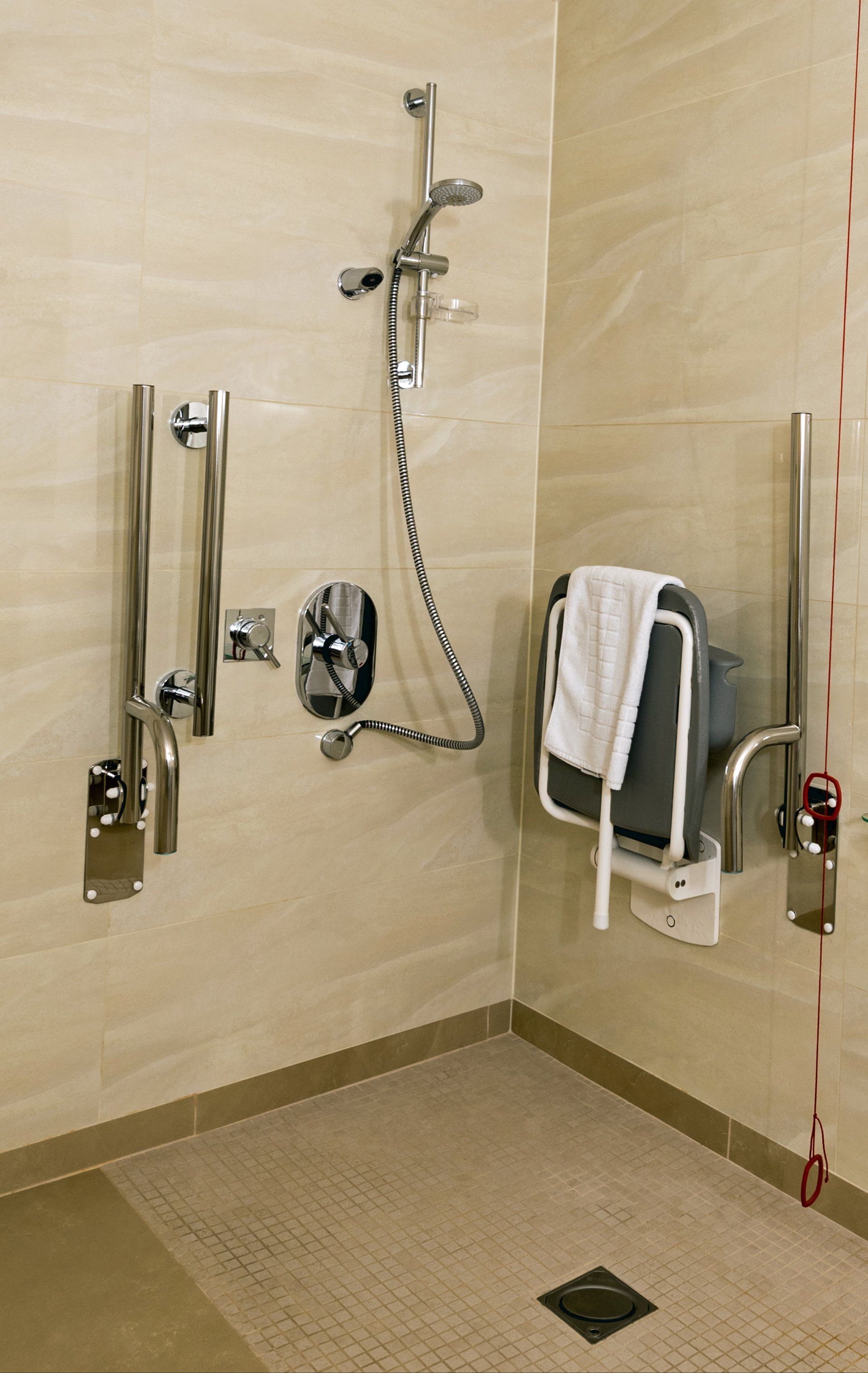 A handicapped shower with a chair and a towel on the floor.