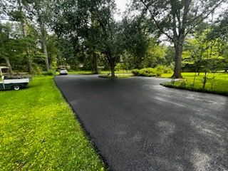 A black asphalt driveway surrounded by trees and grass