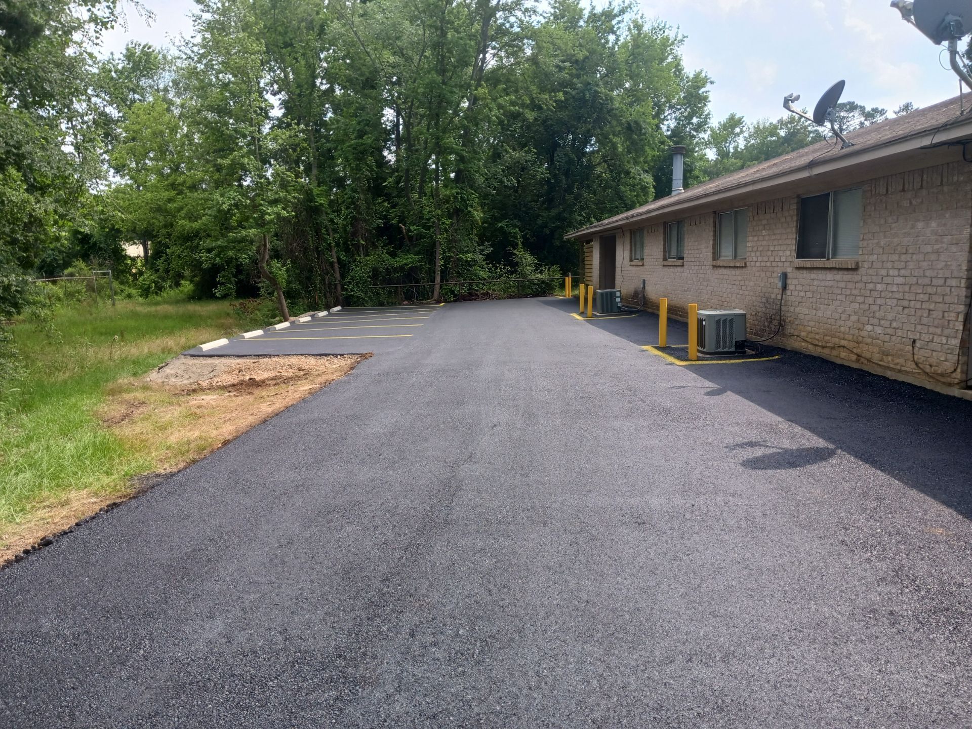 A driveway leading to a brick building with a lot of trees in the background
