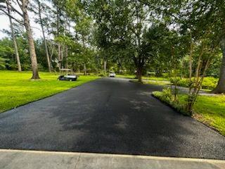 A black asphalt driveway surrounded by trees and grass
