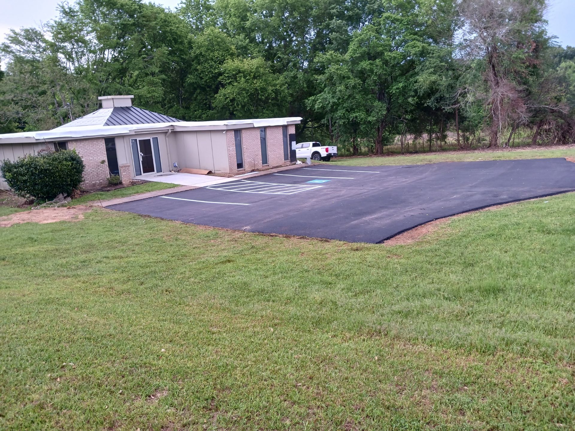 A house is sitting on top of a lush green field next to a parking lot.