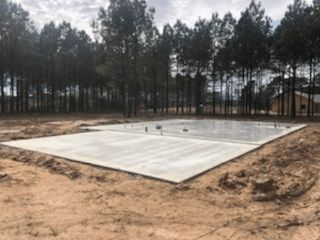 A large concrete slab is sitting in the middle of a dirt field surrounded by trees.