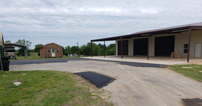 A dirt road leading to a large building with a shed in the background