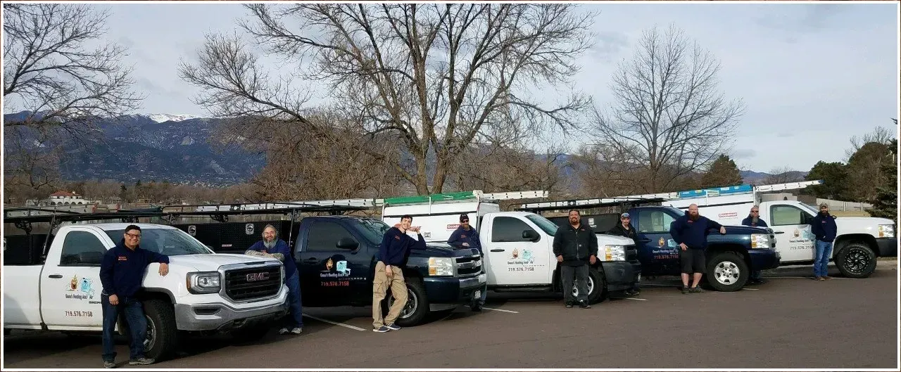 Group of workers standing by their trucks, with mountains and trees in the background.