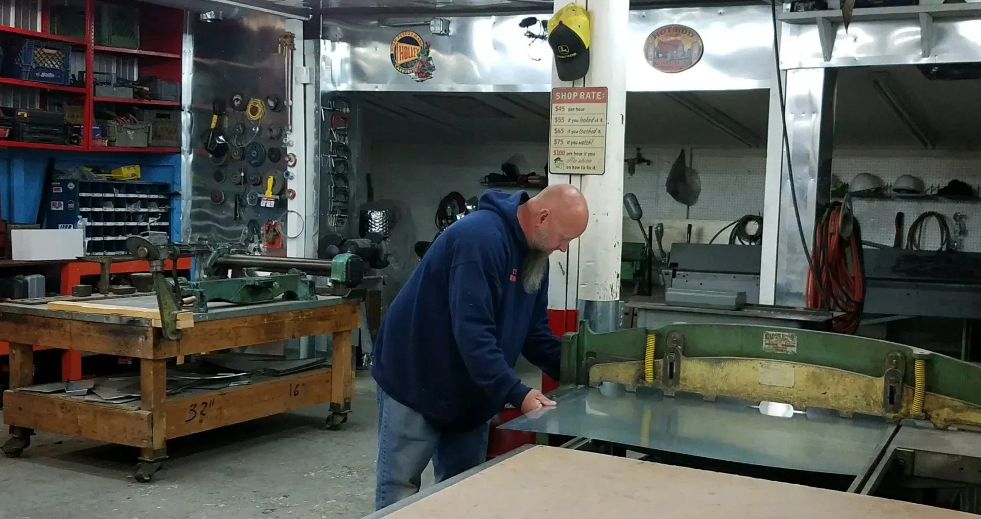 Man cutting metal sheet in a workshop. Tools and equipment visible.