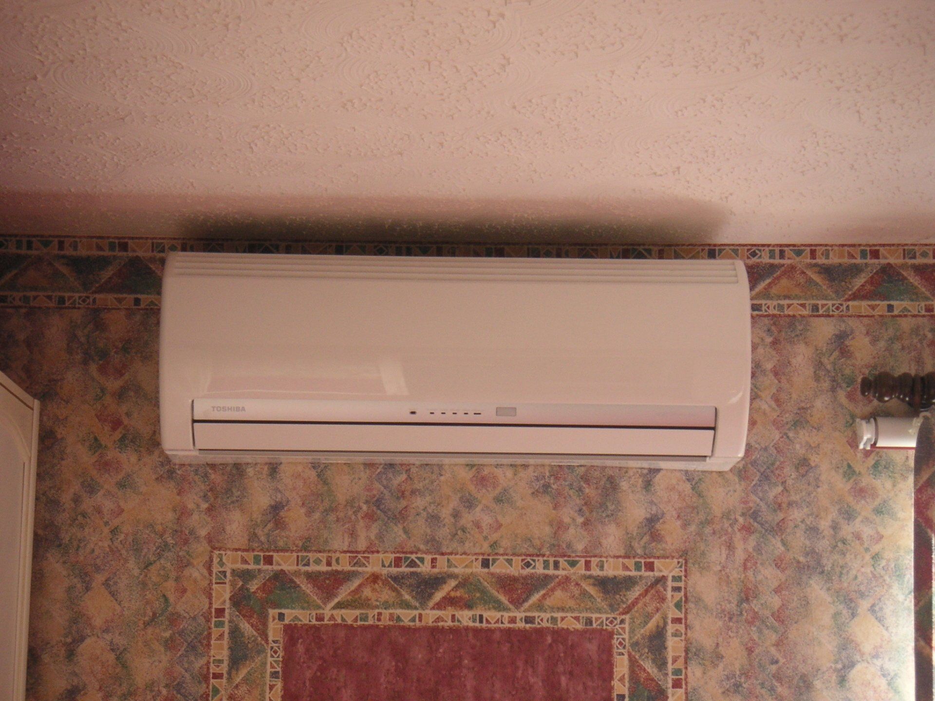 White wall-mounted air conditioner on a patterned wallpapered wall, near a ceiling.