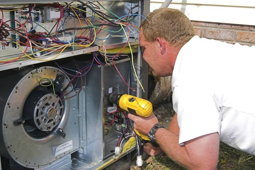 HVAC technician using a drill to work on an air handler unit outdoors.
