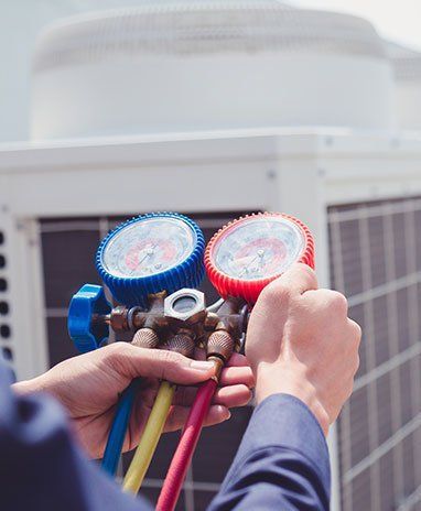 HVAC technician connecting gauges to an AC unit, holding a blue and red manifold with colored hoses, outdoors.