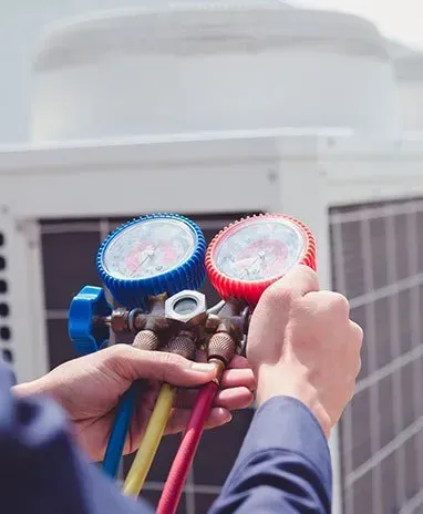 Person using gauges on an air conditioning unit; hands hold a red and blue gauge.