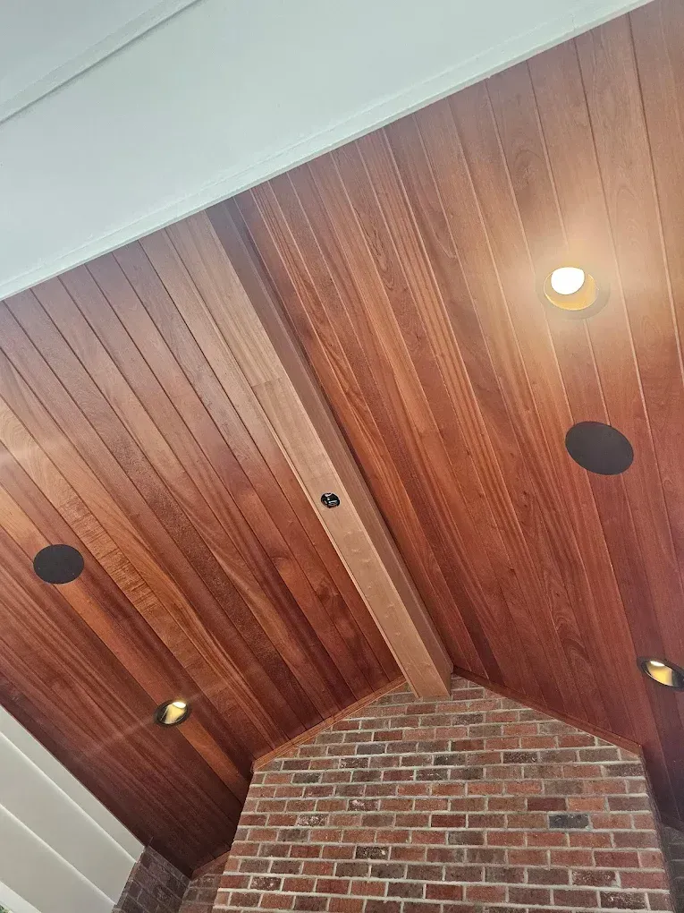 Wooden slatted ceiling with recessed lights and speakers, above a brick fireplace.