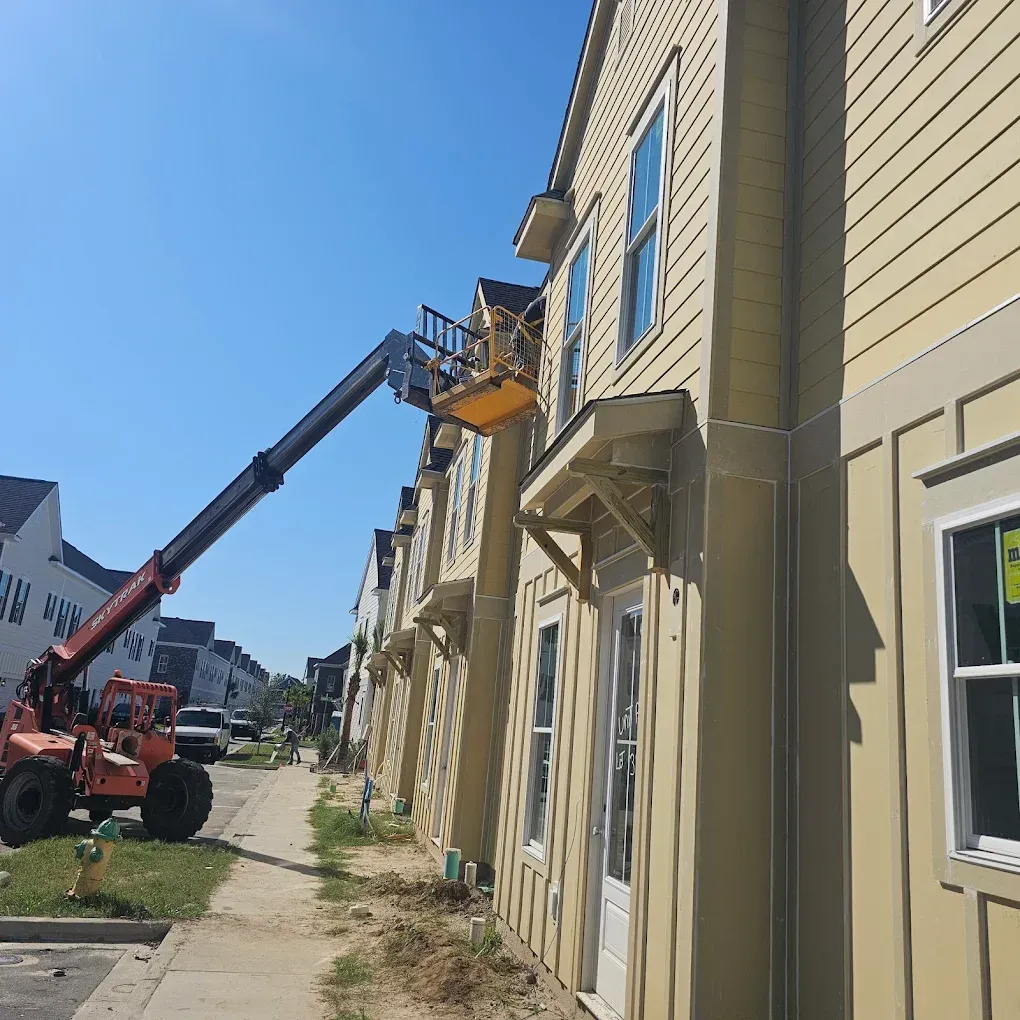 Construction worker in a lift basket repairing siding on a multi-story building. Sunny day.