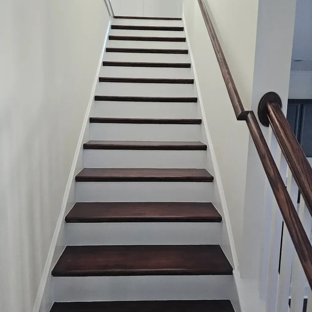 Staircase with dark brown steps and white risers, wooden handrail on the right, leading upwards.