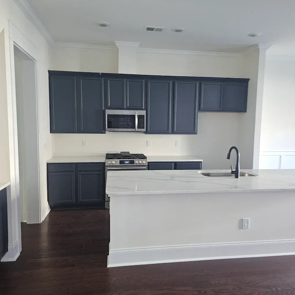 Blue cabinets and white island in a kitchen, stainless steel appliances, dark wood floor.