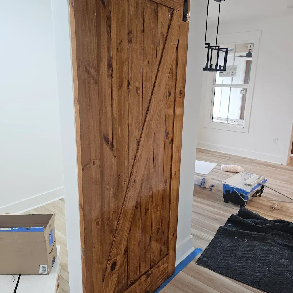Narrow hallway with dark wood floors, white walls, and closed doors. A window is at the end of the hall.
