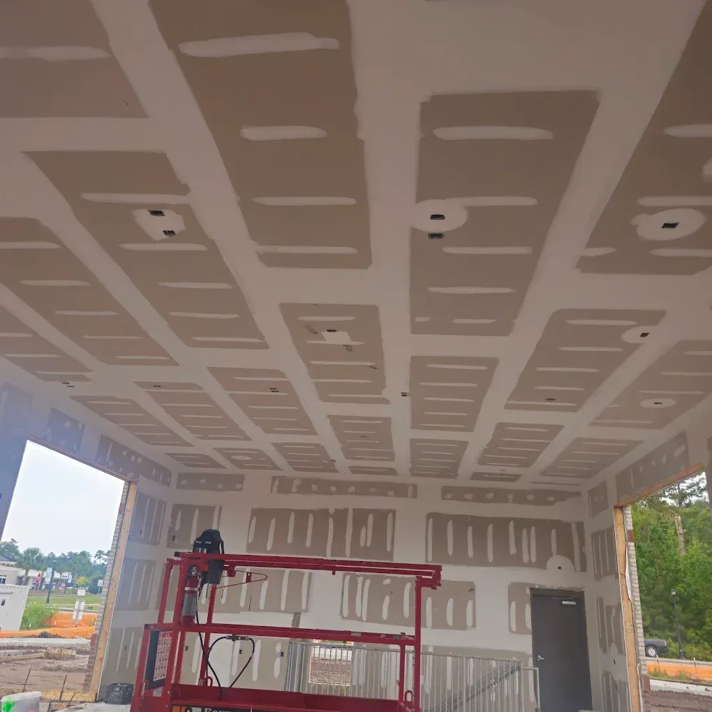 Construction site interior: drywall installed on ceiling and walls, with lift in foreground.