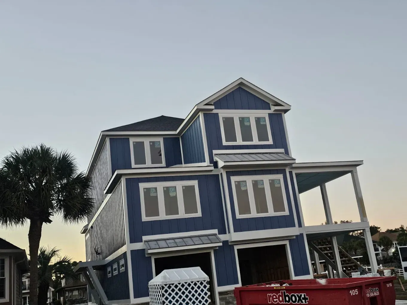 Blue multi-story house under construction with white trim, near a palm tree.
