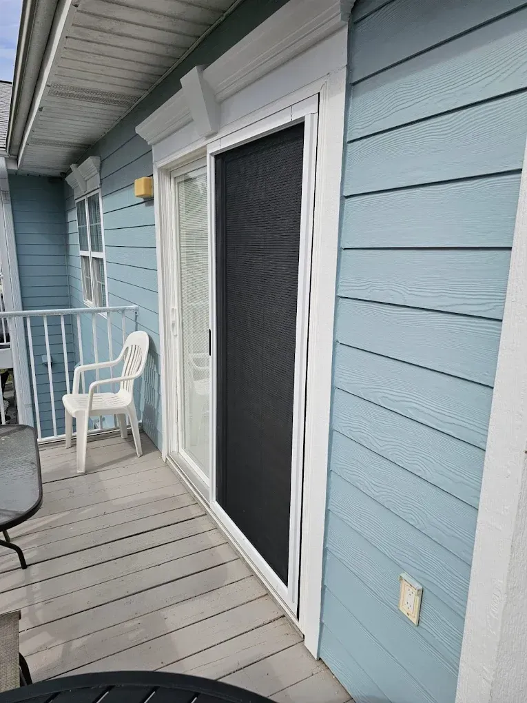 Sliding glass door with screen on a light blue building's balcony.