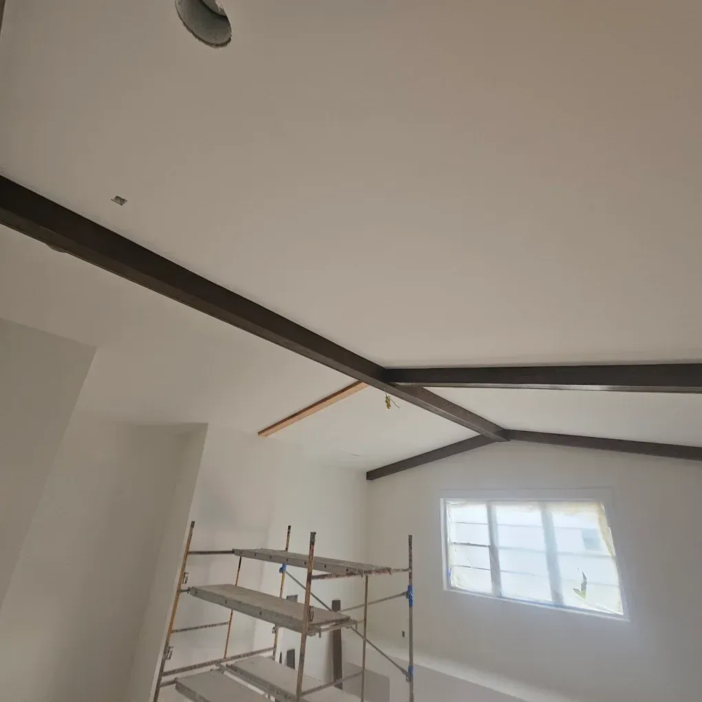 Interior room with white walls, exposed dark beams on ceiling, scaffolding, and a window.