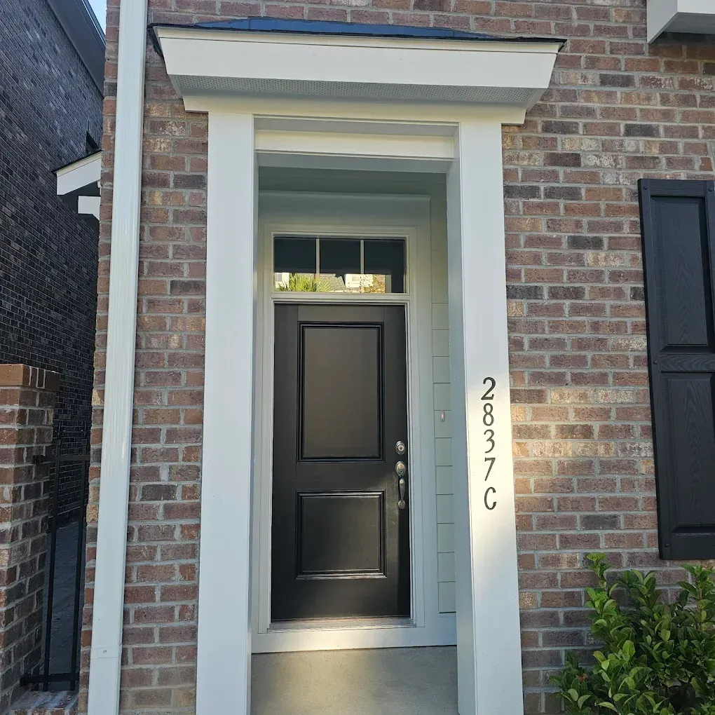 Front door of a brick home with white trim and a black door. Address is visible on the side.