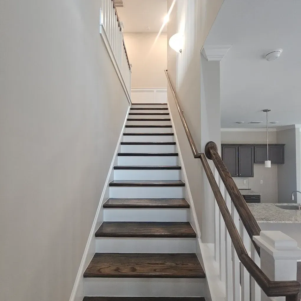 Staircase with dark wood treads and white risers, leading upwards. Wooden handrail on the right.