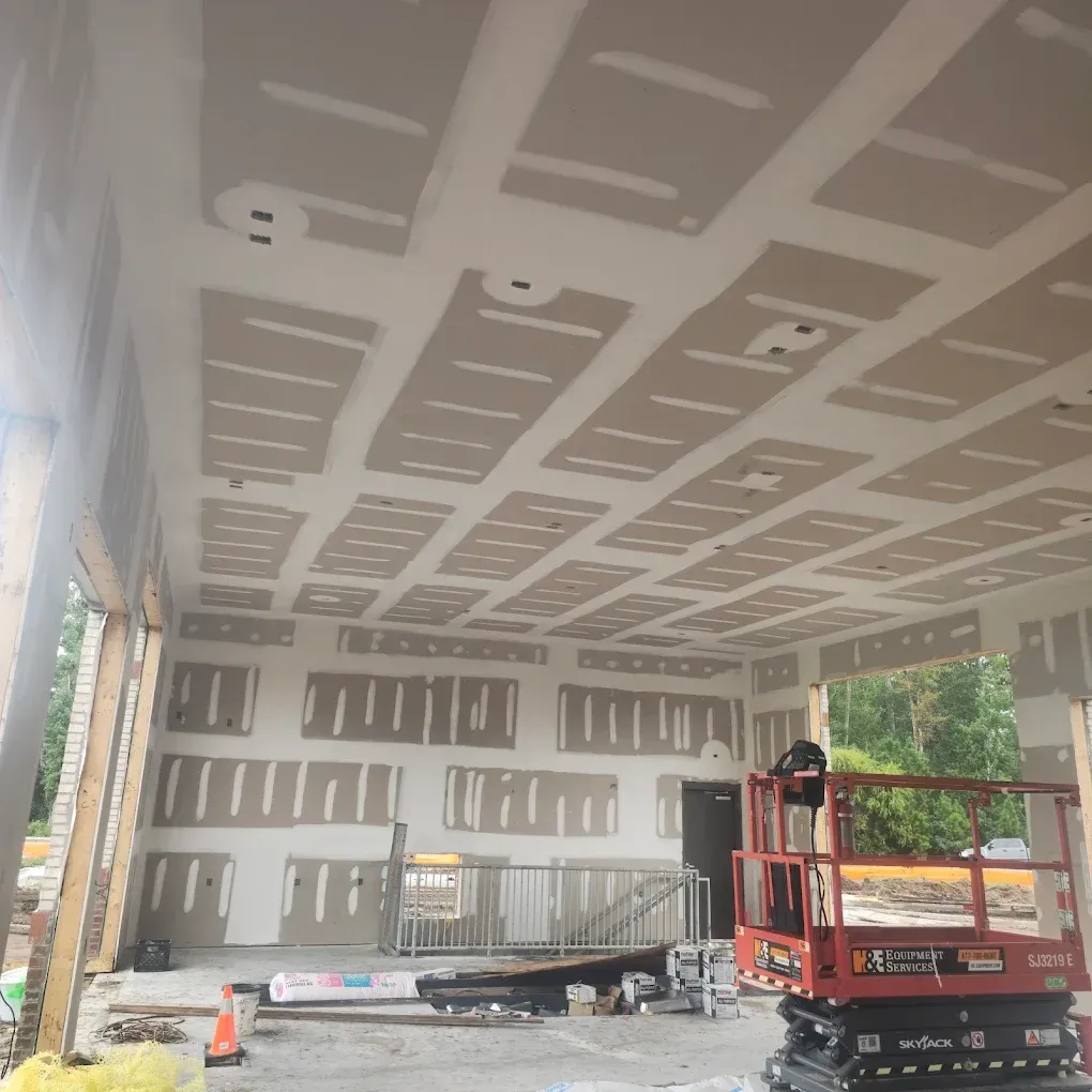Construction site interior; drywall panels installed on ceiling and walls; lift present.