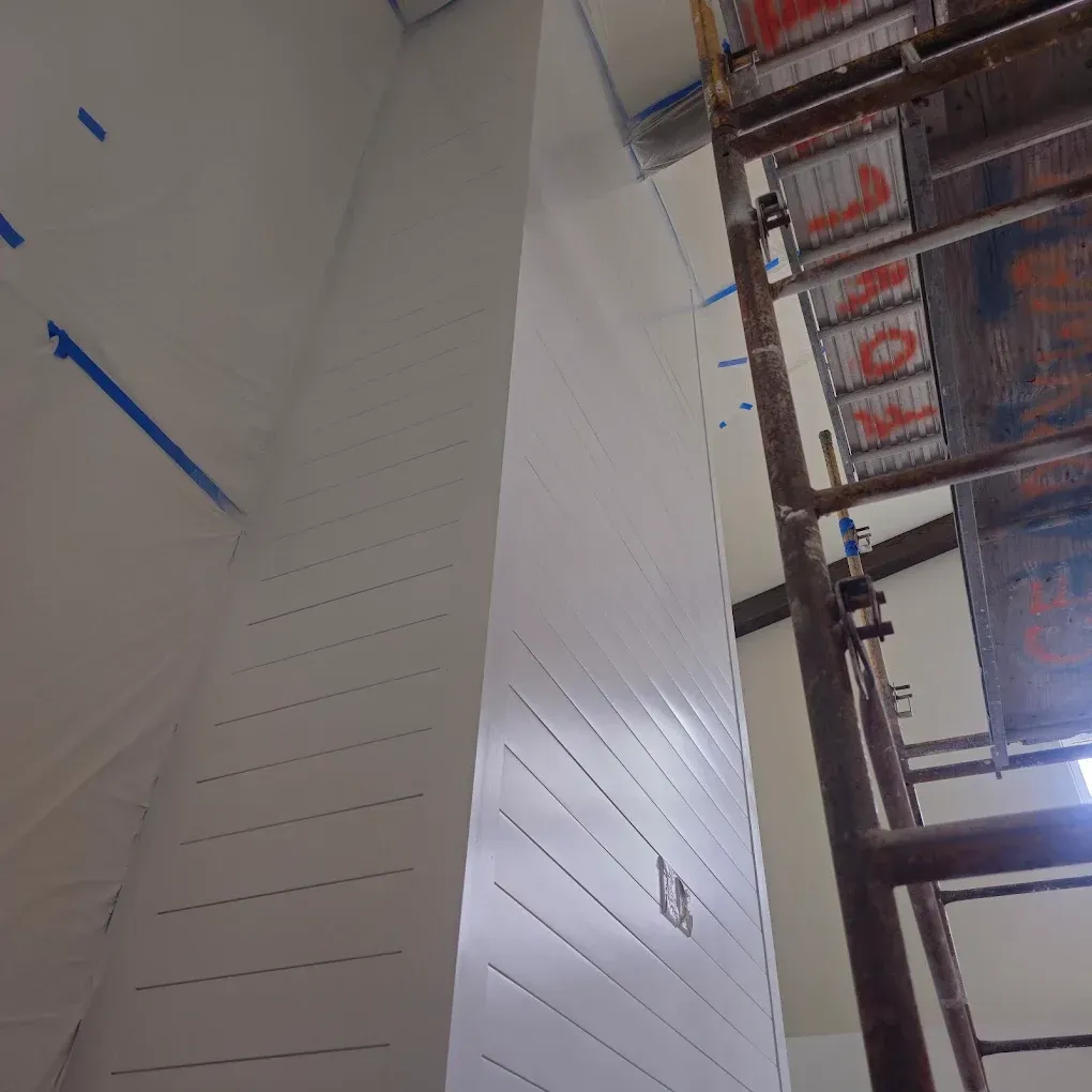 White wall with horizontal grooves, blue tape, and a scaffolding.