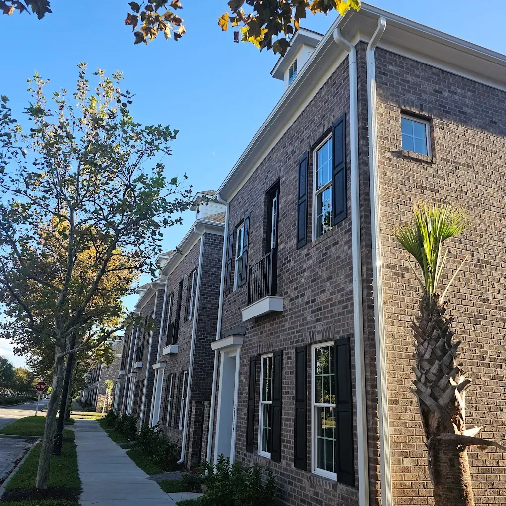 Row of brick townhouses with black shutters and a sidewalk on a sunny day.