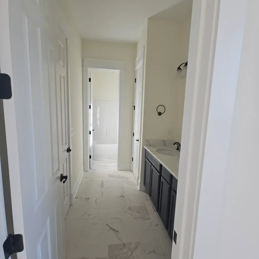 Hallway with white walls, doors, and marble-look floor; black vanity and door hardware.