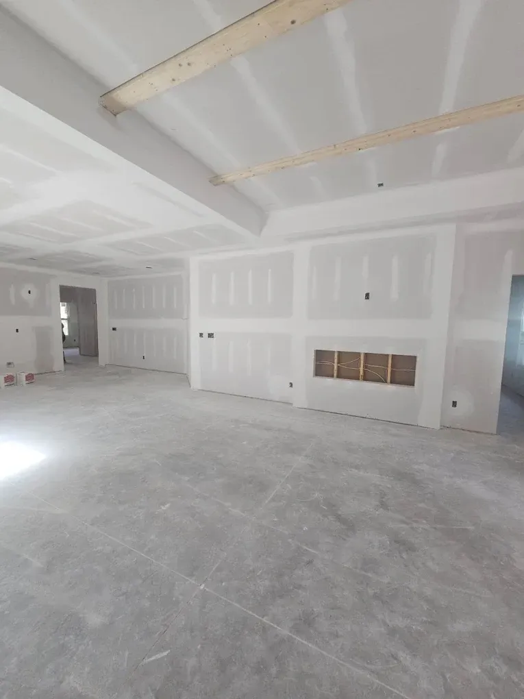 Interior of a new home under construction, with drywall on walls and ceiling, exposed beams, and a concrete floor.