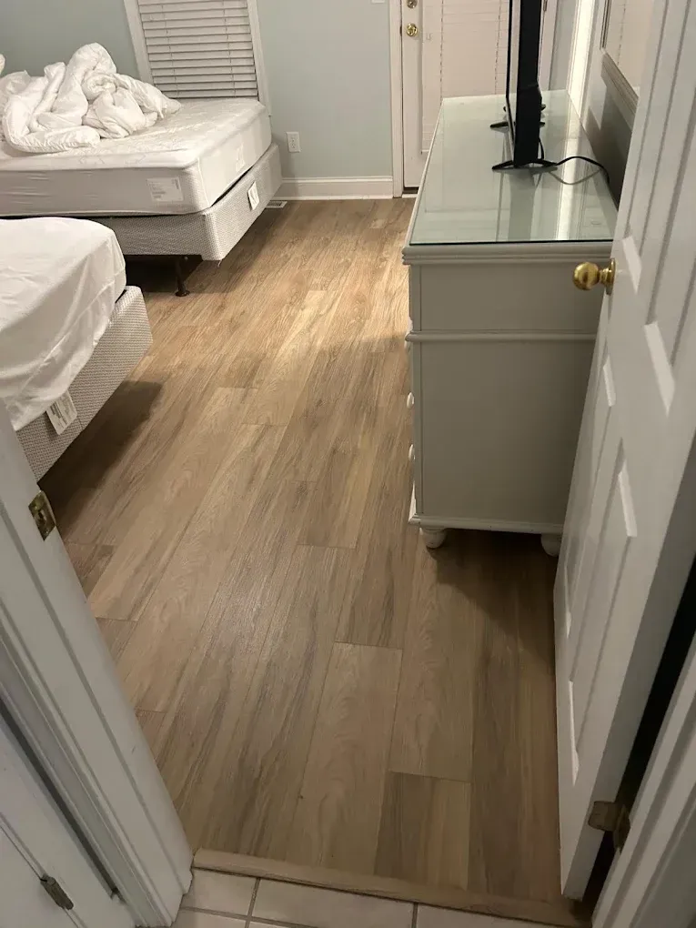 Bedroom with light wood-look flooring, two beds, and a white dresser with a television.